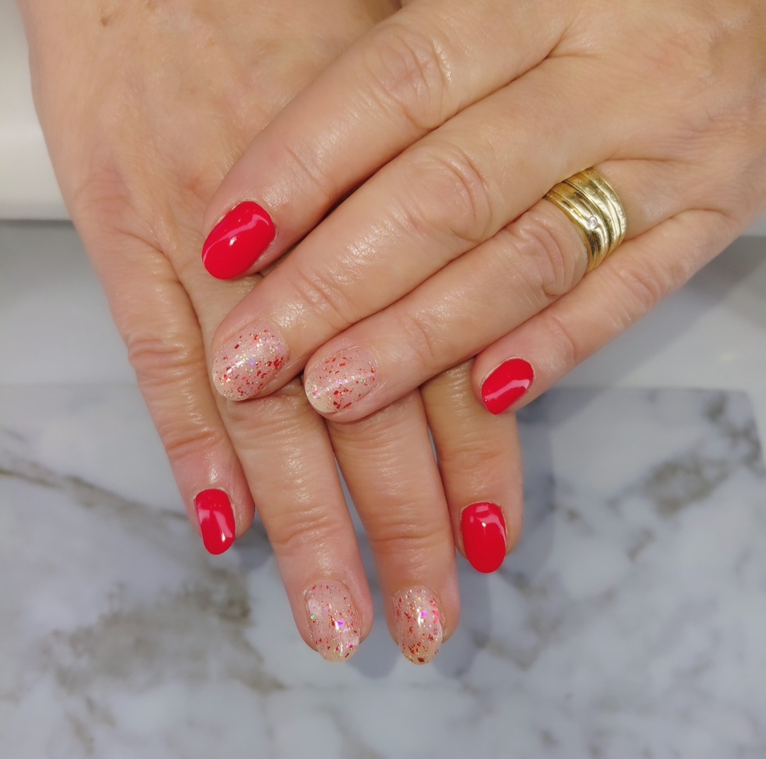 Rode gelnagels met glitteraccenten, handen op een marmeren tafel