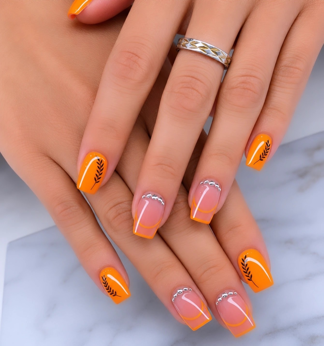 Oranje square gelnagels met strass en blaadjes, op marmer