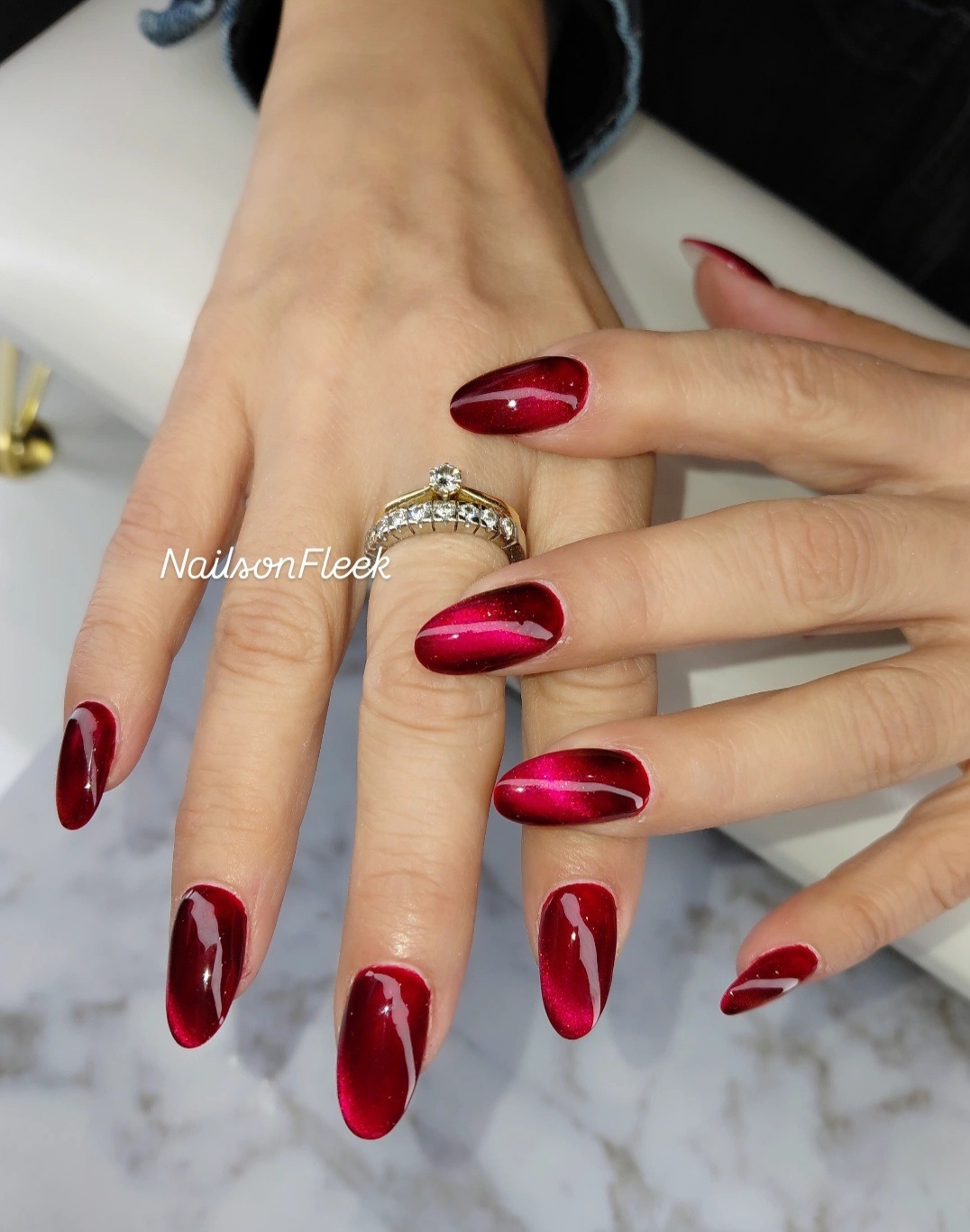 Dieprode cat-eye gelnagels op een hand met ring, op een marmeren tafel