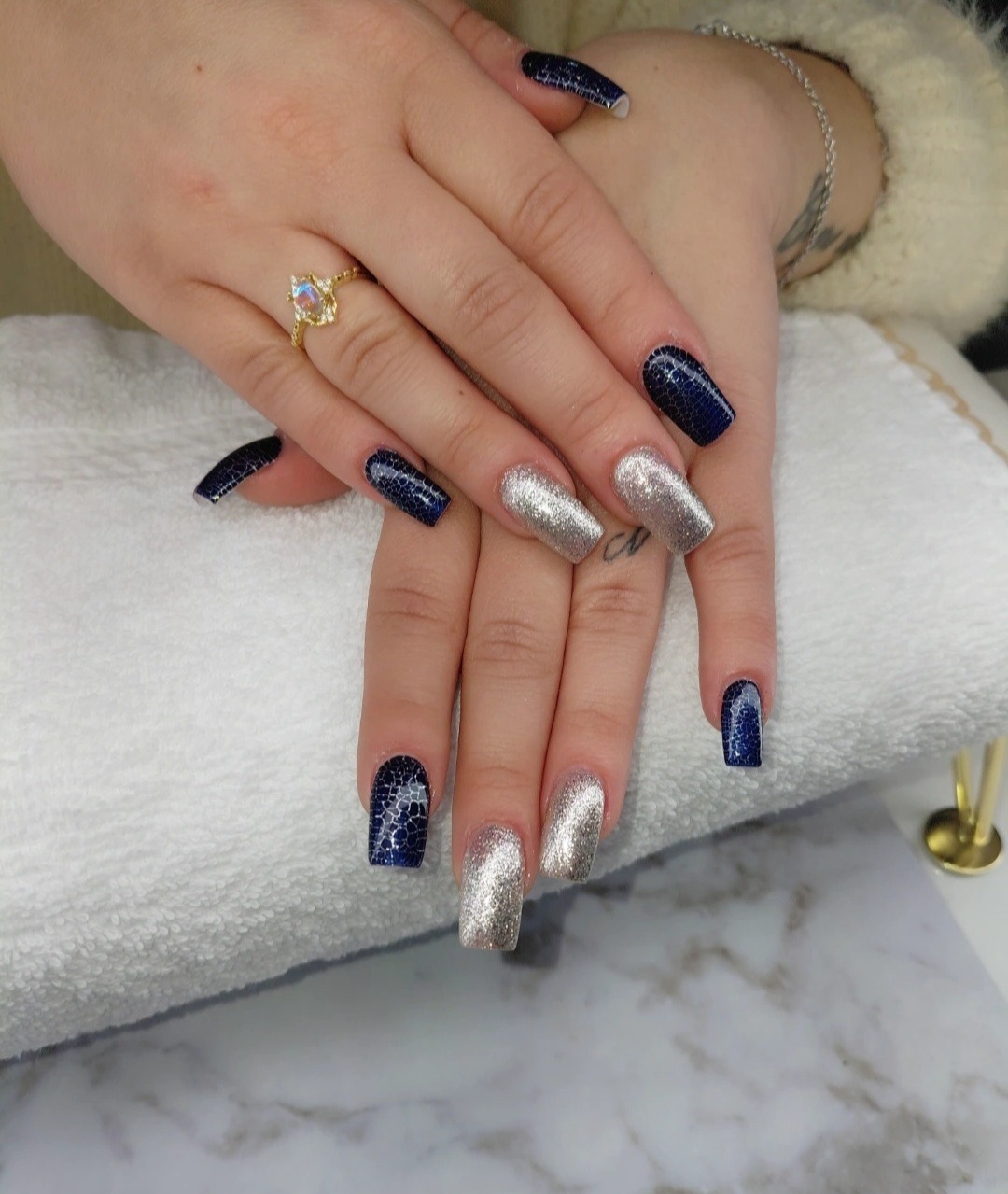 Navy gelnagels met zilverglitter accentnagels op een witte handdoek